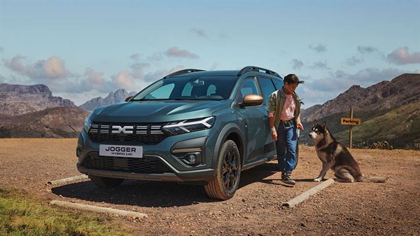 מבט מלפנים על דאצ'יה ג'וגר חונה בטבע הררי לצד אישה וכלב